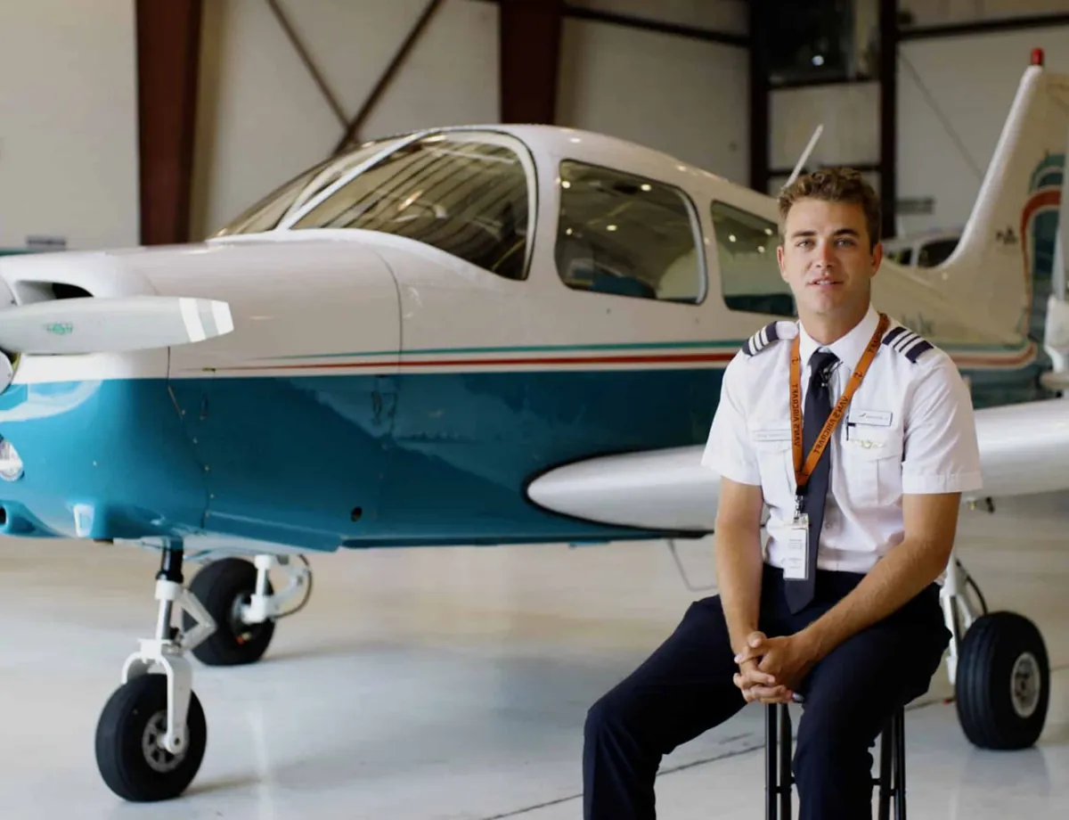 Pilot seated beside a training aircraft in the hangar